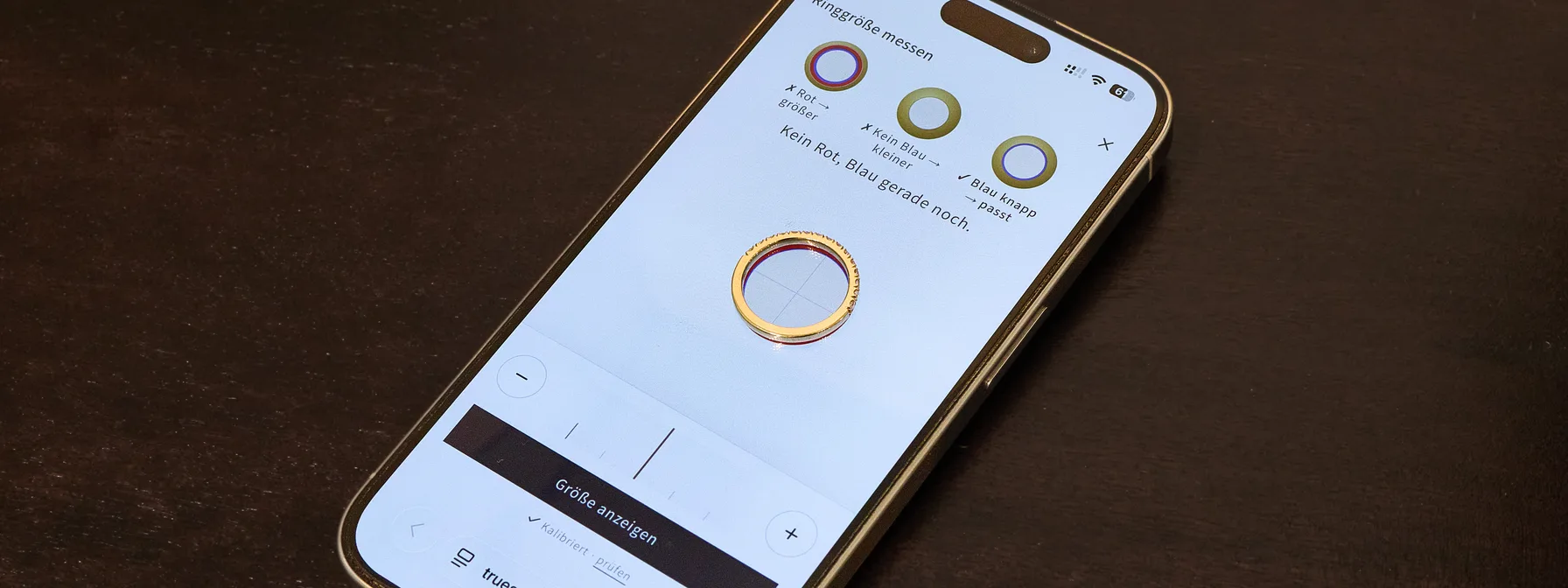 Smartphone auf dem Tisch mit dem Ringgrößen-Tool von Truestones, ein Goldring mit Diamanten liegt auf dem Messkreis am Bildschirm