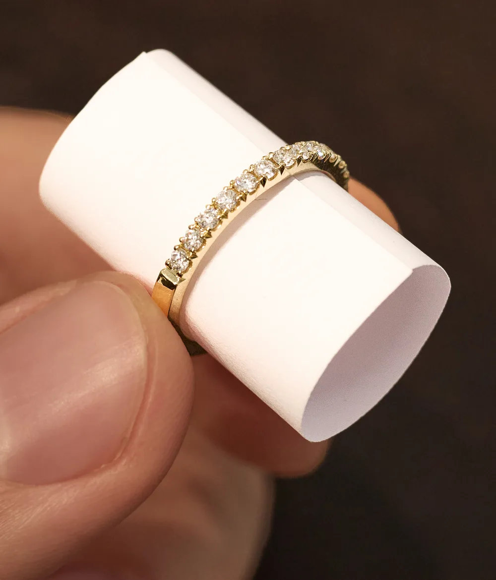 Ein eng gerollter Papierstreifen steckt in einem schmalen Goldring mit Diamanten und liegt innen an